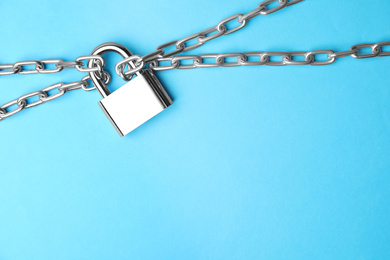 Photo of Steel padlock, chains and space for text on light blue background, top view. Safety concept