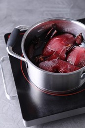 Tasty red wine poached pears and spices in pot on grey table, closeup