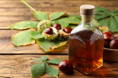 Chestnuts, leaves and bottle of essential oil on wooden table. Space for text