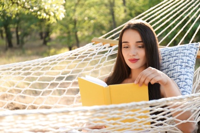 Photo of Young woman reading book in comfortable hammock at green garden