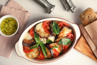 Flat lay composition with baked eggplant, tomatoes and basil in dishware on wooden table