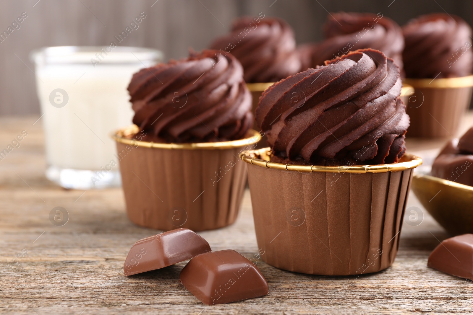 Photo of Delicious cupcakes and chocolate pieces on wooden table, closeup