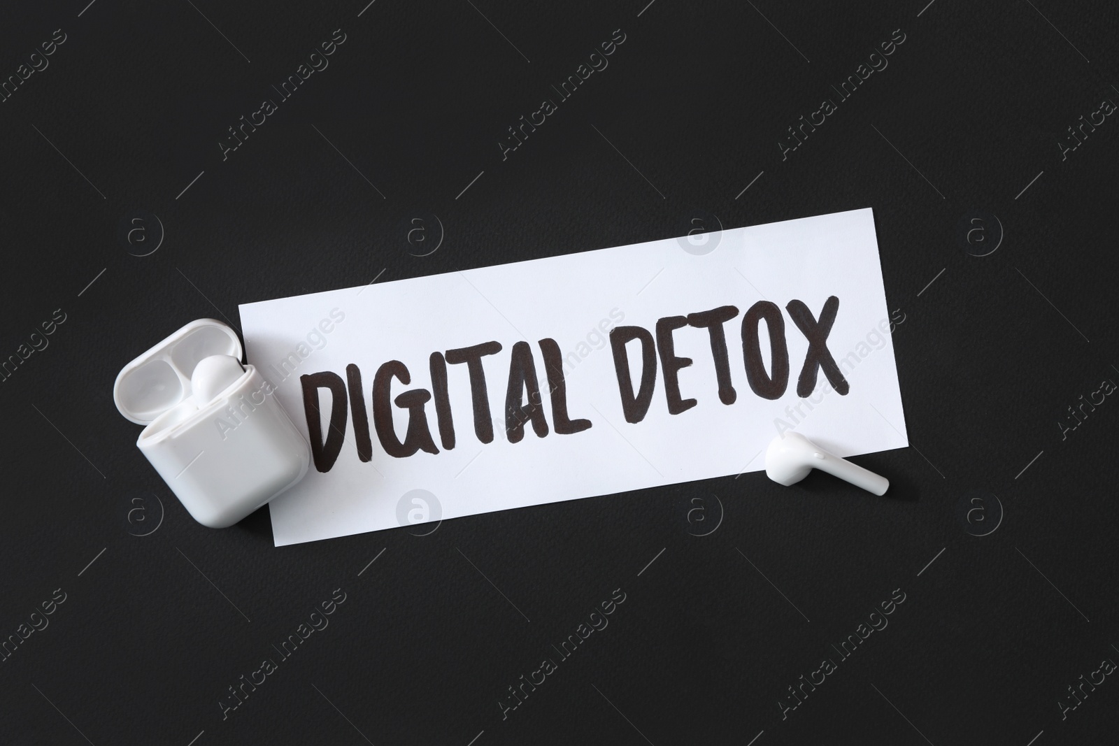 Photo of Paper note with phrase DIGITAL DETOX and earphones on black background, flat lay