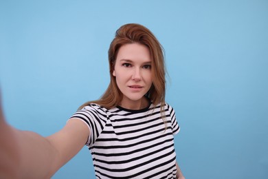 Beautiful woman taking selfie on light blue background