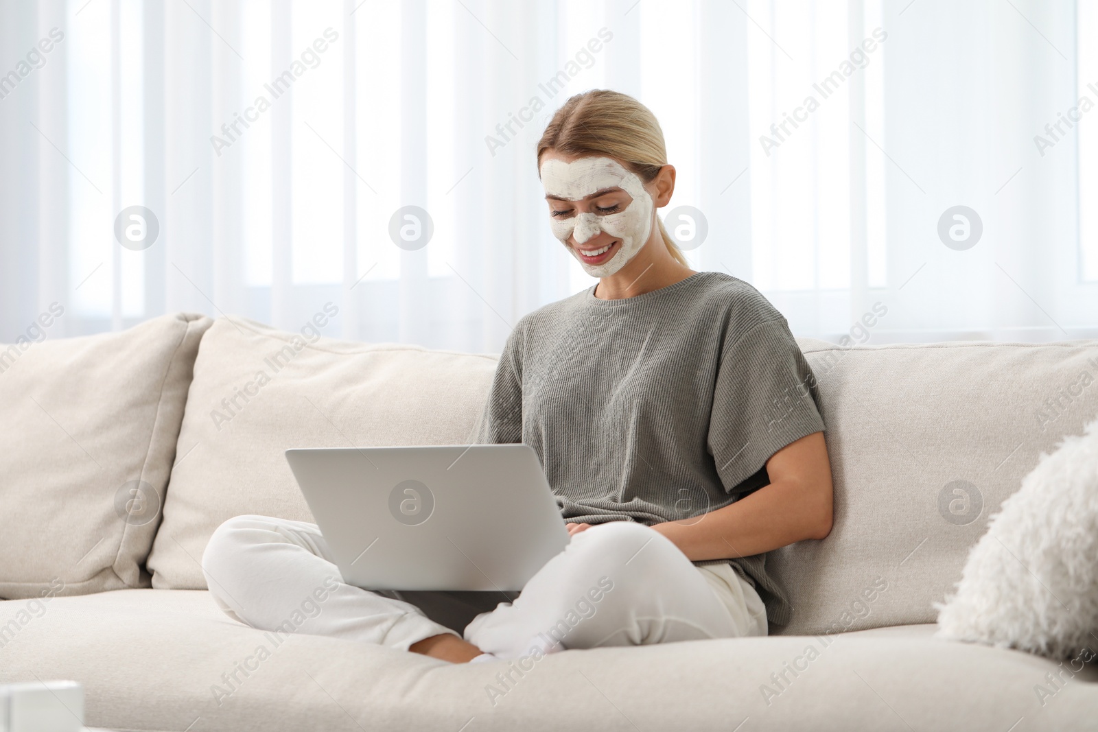 Photo of Young woman with face mask using laptop on sofa at home. Spa treatments