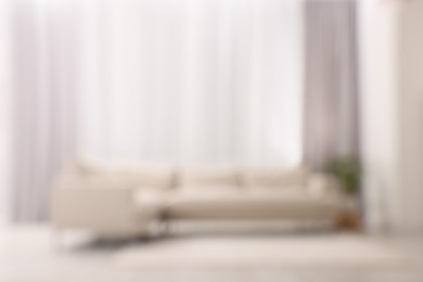 Photo of Blurred view of comfortable sofa and window with beautiful curtains in room. Interior design