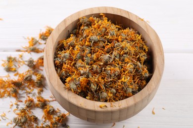 Photo of Dry calendula flowers in bowl on white wooden table, closeup