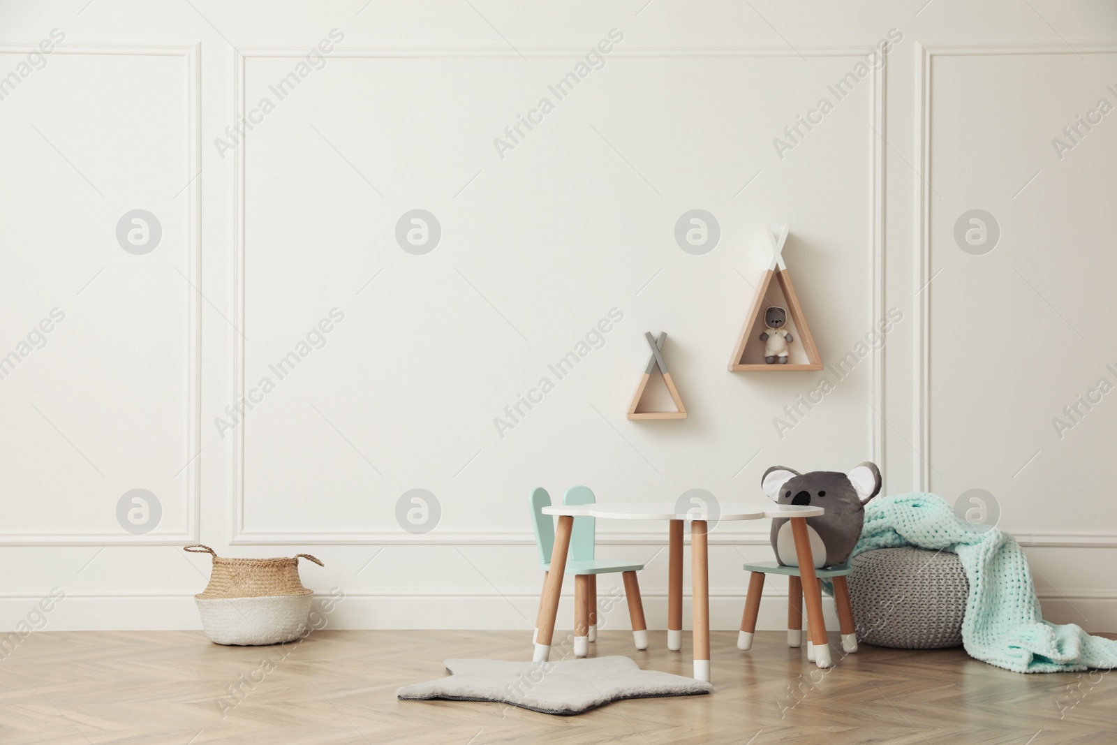 Photo of Cute child room interior with furniture, toys and wigwam shaped shelves on white wall