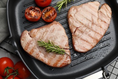 Delicious tuna steaks with rosemary and tomatoes on table, flat lay