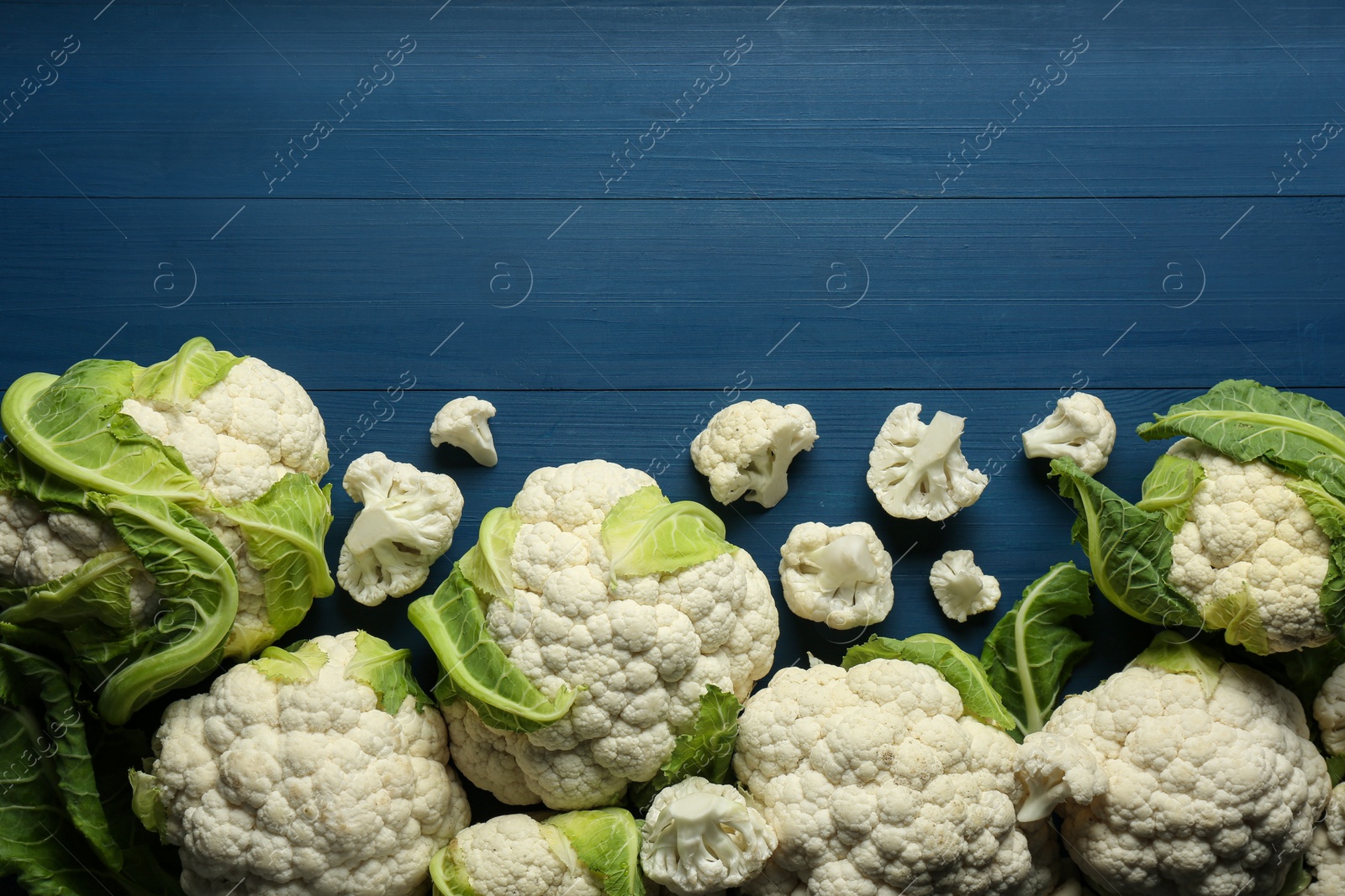 Photo of Fresh whole and cut cauliflowers on blue wooden table, top view. Space for text