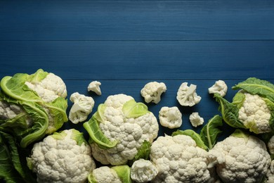 Fresh whole and cut cauliflowers on blue wooden table, top view. Space for text