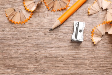 Photo of Sharpeners, pencil and shavings on wooden table, flat lay. Space for text