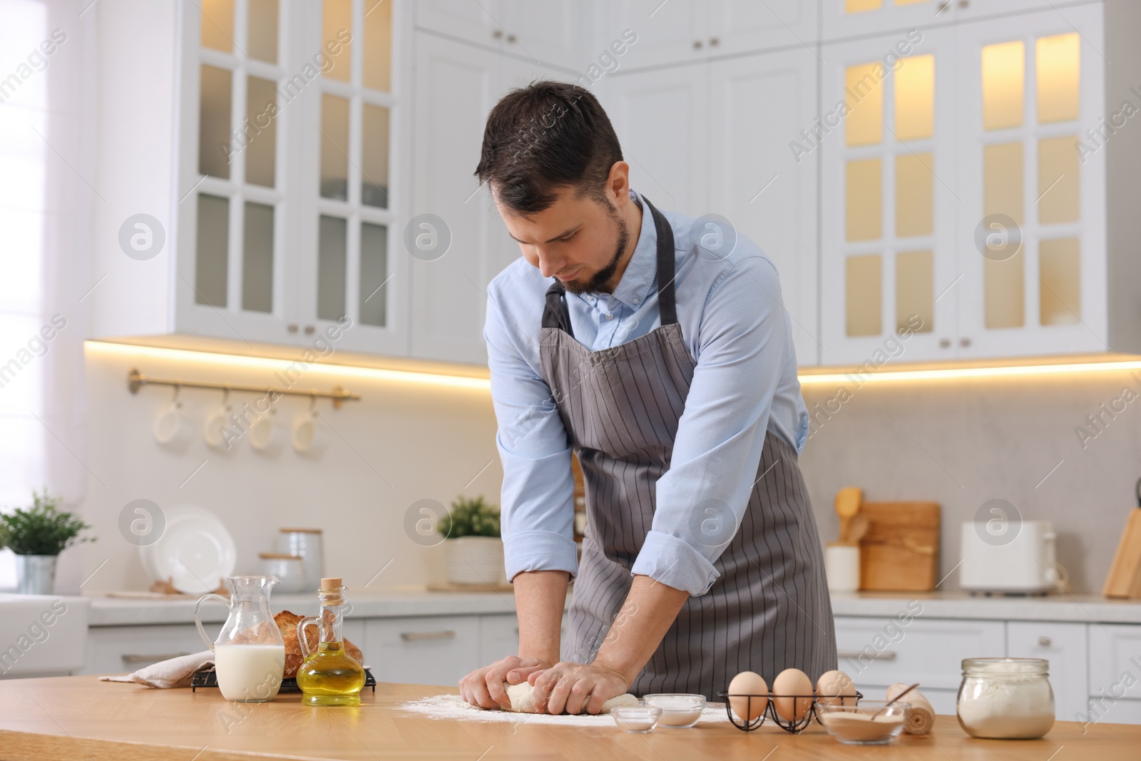 Photo of Making bread. Man kneading dough at wooden table in kitchen