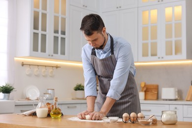 Making bread. Man kneading dough at wooden table in kitchen