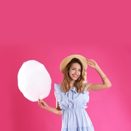 Happy young woman with cotton candy on pink background