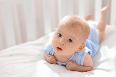 Cute little baby lying in crib at home, space for text