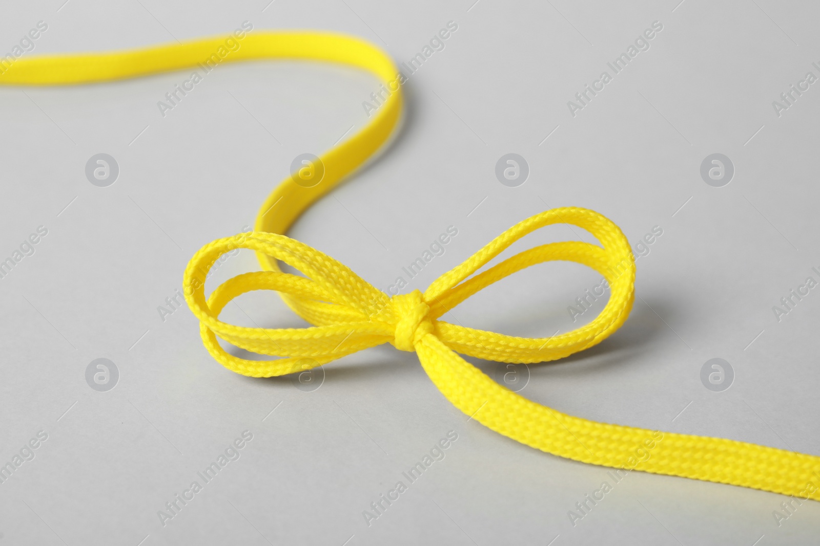 Photo of Yellow shoe lace tied in bow on light grey background