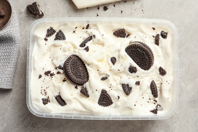 Photo of Container of ice cream and chocolate cookies on grey background, top view