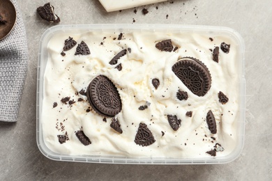 Container of ice cream and chocolate cookies on grey background, top view