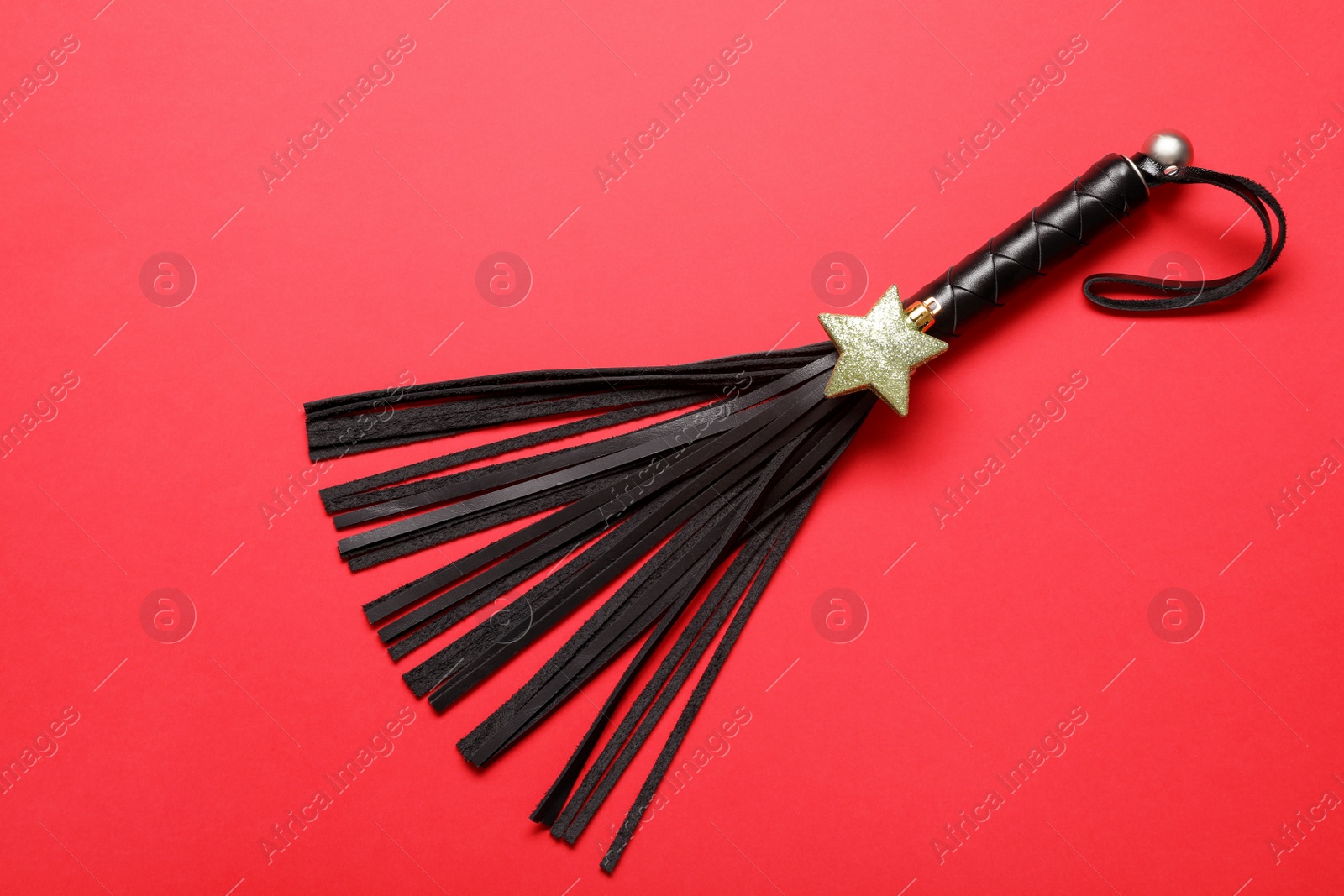 Photo of Black whip for sexual role play and gold star on red background, top view