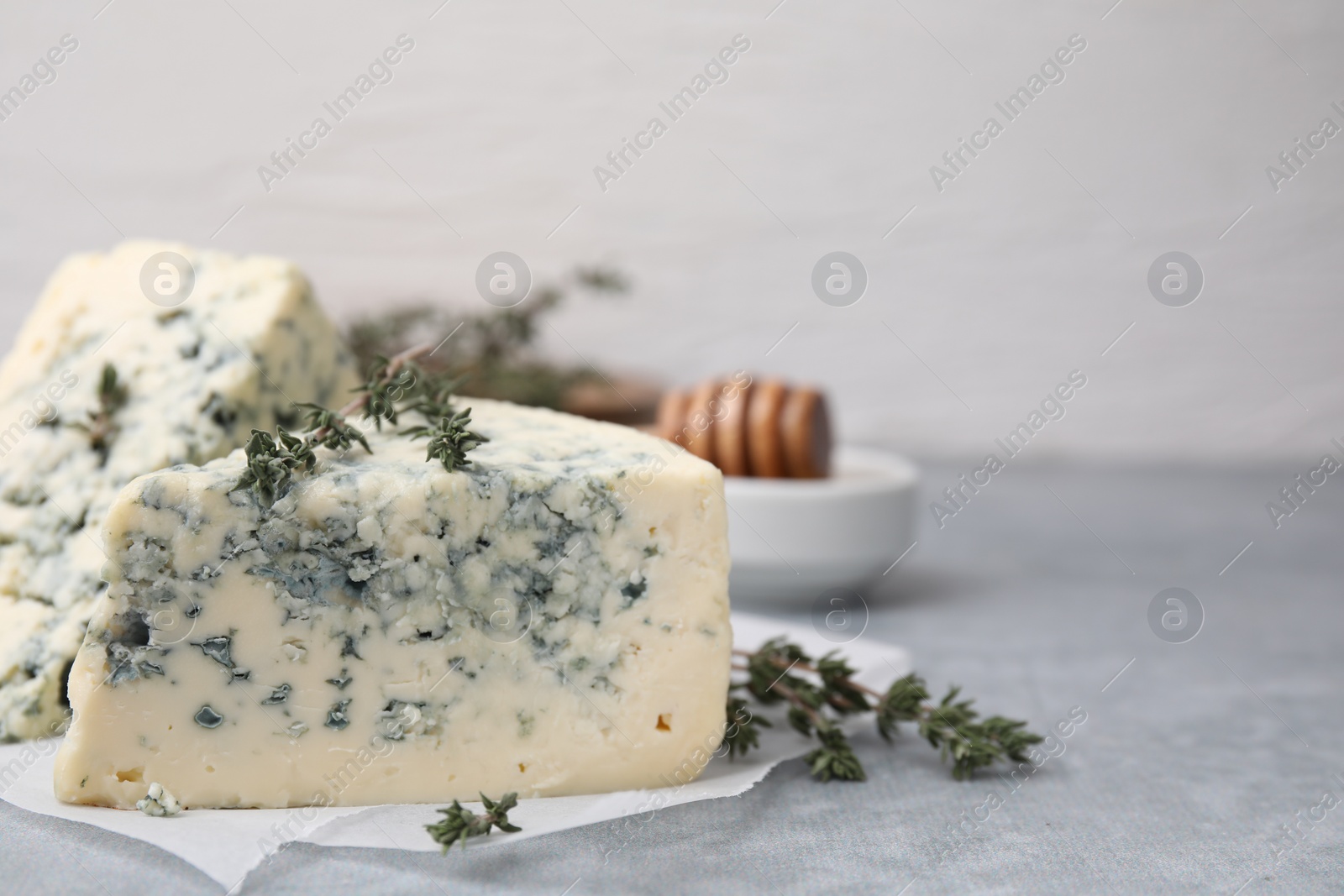 Photo of Tasty blue cheese with thyme on grey table, closeup. Space for text