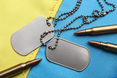 Photo of Bullets and military ID tags on Ukrainian flag, flat lay