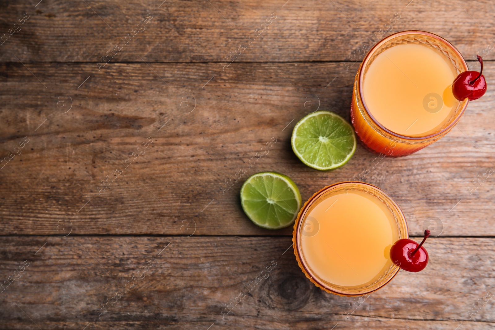 Photo of Fresh alcoholic Tequila Sunrise cocktails on wooden table, flat lay. Space for text
