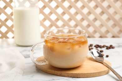 Photo of Refreshing iced coffee with milk in glass cup and spoon on white table