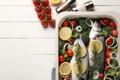 Photo of Raw fish with lemon in baking dish and vegetables on white wooden table, flat lay. Space for text