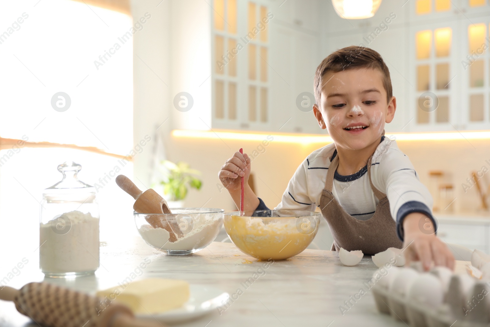 Photo of Cute little boy cooking dough at table in kitchen