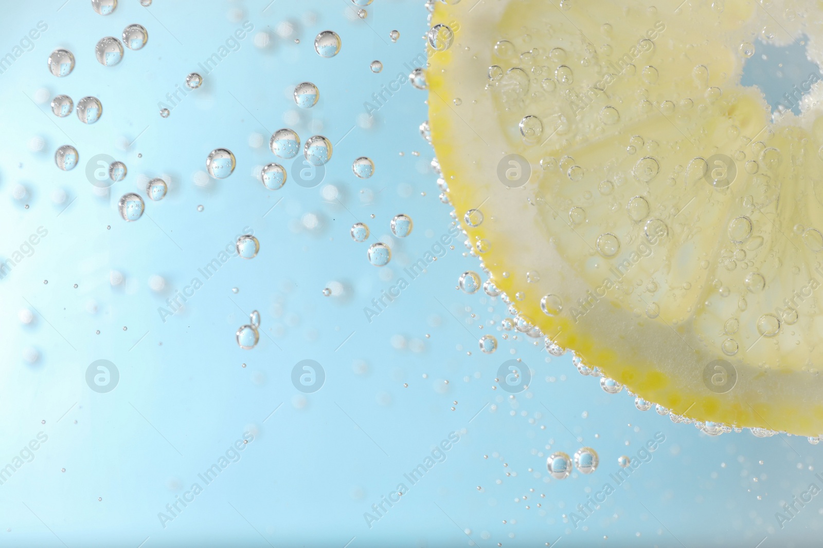 Photo of Juicy lemon slice in soda water against light blue background, closeup. Space for text