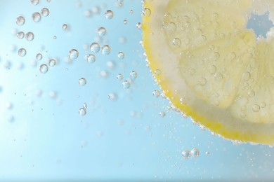 Photo of Juicy lemon slice in soda water against light blue background, closeup. Space for text