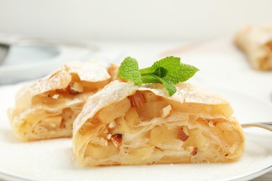 Photo of Pieces of delicious apple strudel with almonds, powdered sugar and mint on plate, closeup