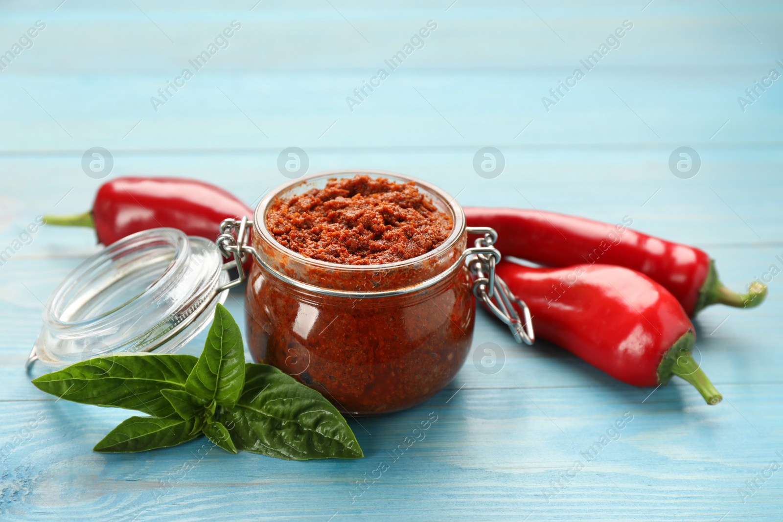 Photo of Delicious adjika sauce in glass jar and ingredients on light blue wooden table
