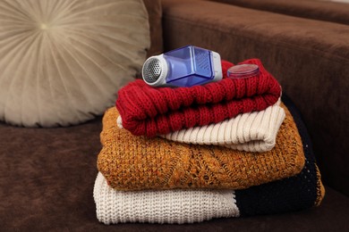 Photo of Modern fabric shaver and knitted clothes on brown sofa