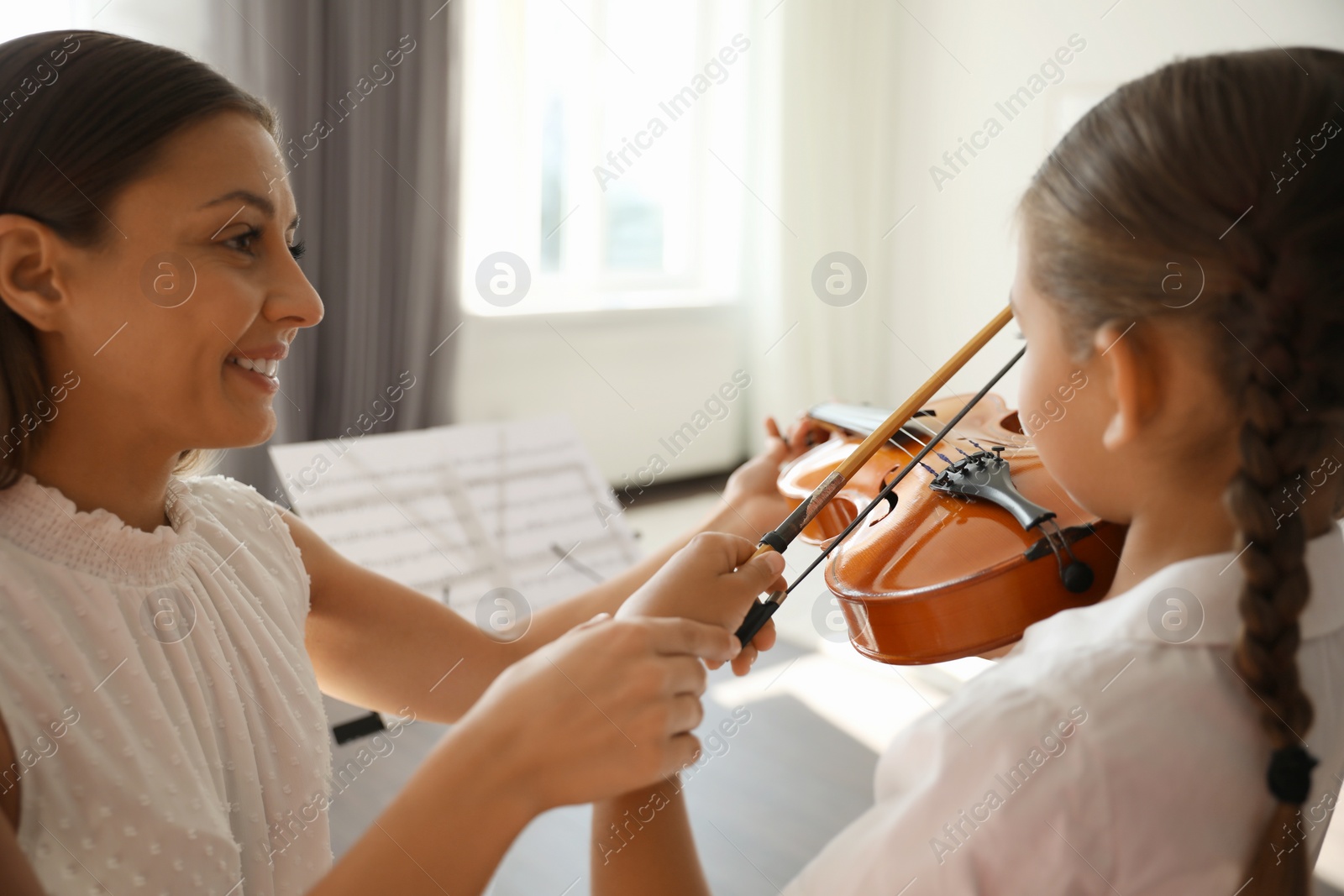 Photo of Young woman teaching little girl to play violin indoors