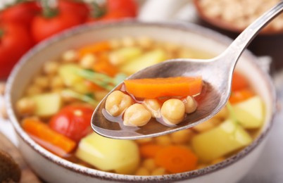 Photo of Taking tasty chickpea soup in spoon above bowl, closeup