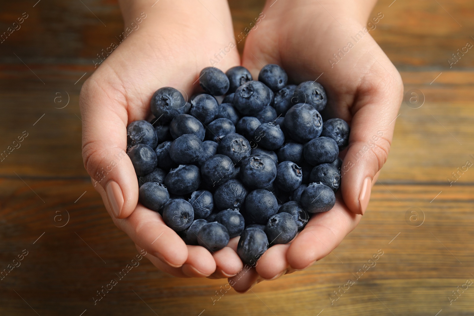 Photo of Woman holding juicy fresh blueberries at wooden table, closeup