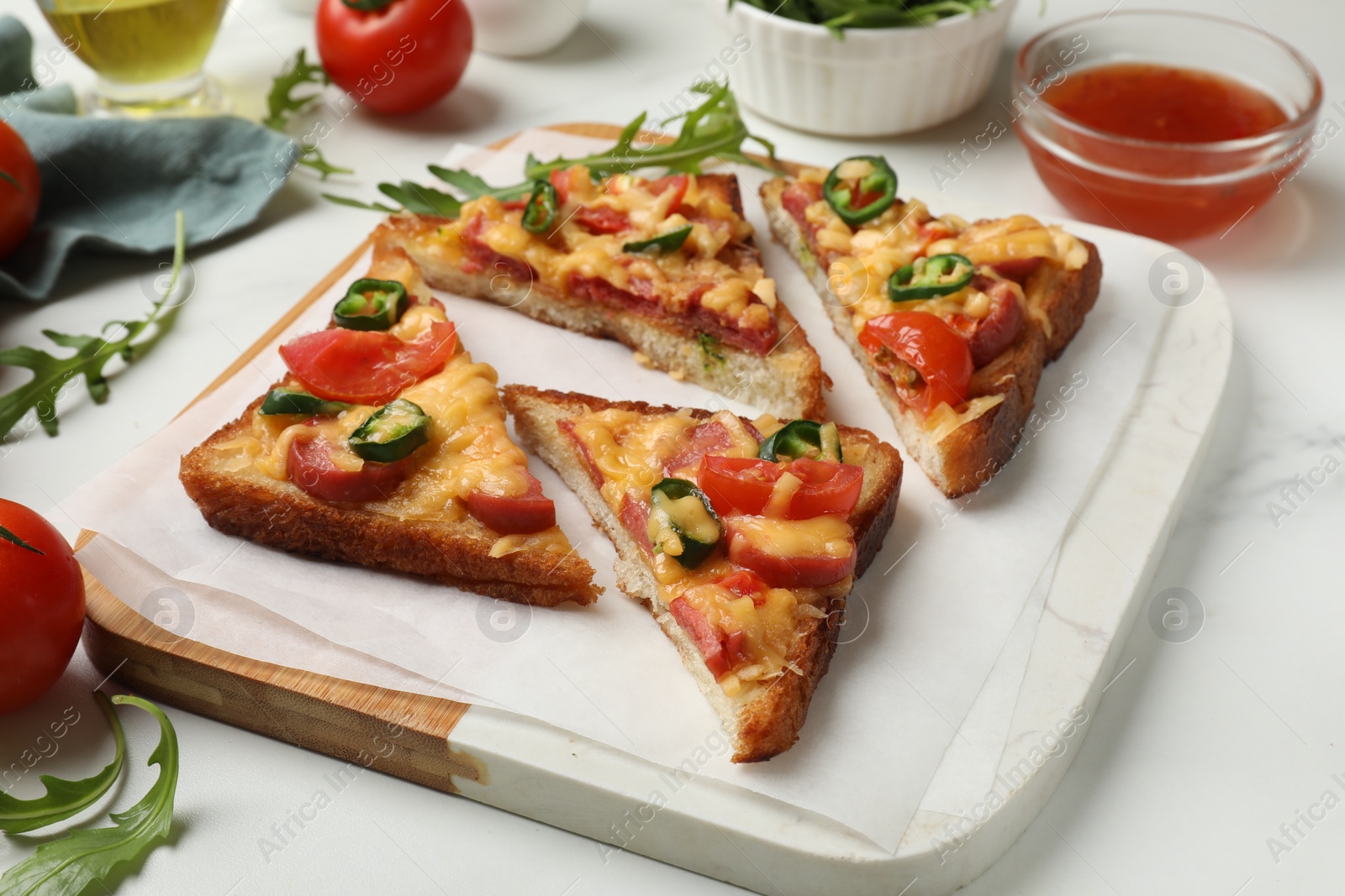 Photo of Tasty pizza toasts and ingredients on white marble table, closeup