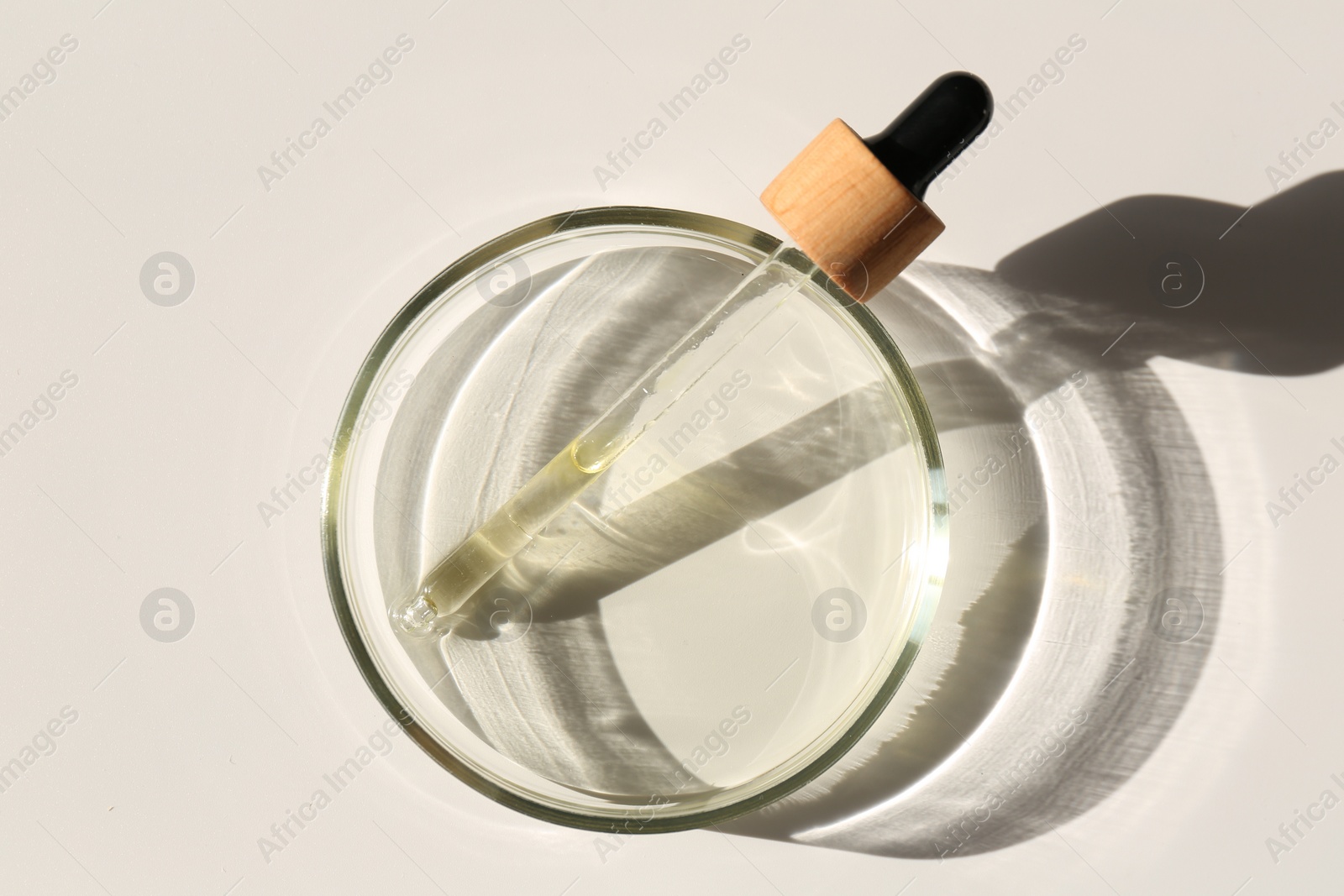 Photo of Petri dish with liquid sample and pipette on light background, top view