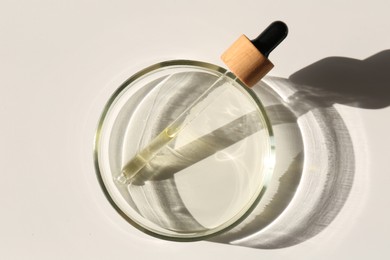 Photo of Petri dish with liquid sample and pipette on light background, top view