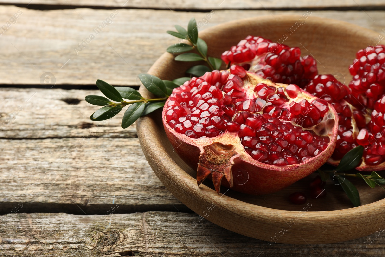 Photo of Cut fresh pomegranate and green leaves on wooden table, closeup. Space for text