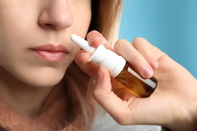 Photo of Sick young woman using nasal spray on light blue background, closeup