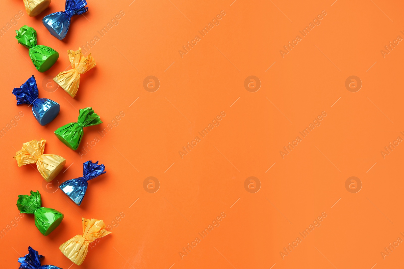 Photo of Many candies in colorful wrappers on orange background, flat lay. Space for text