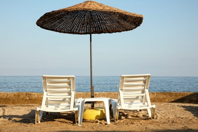 Two lounge chairs and beach umbrella on sea shore