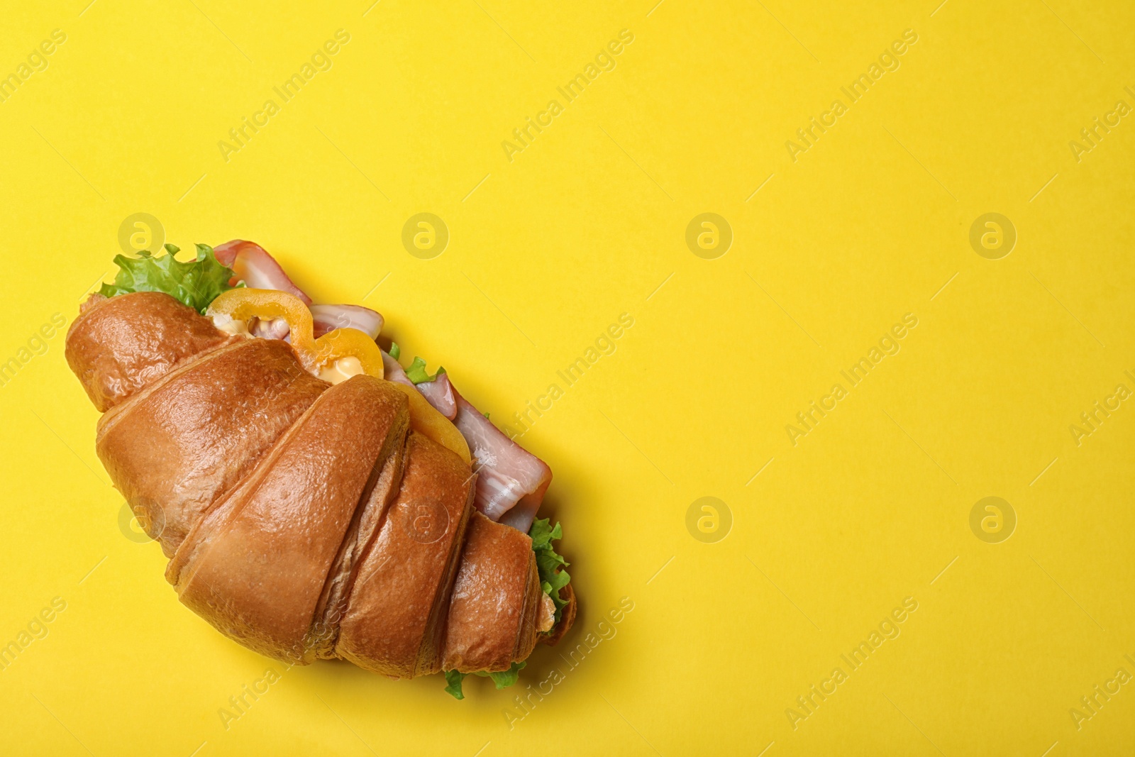 Photo of Tasty croissant sandwich with ham on yellow background, top view. Space for text