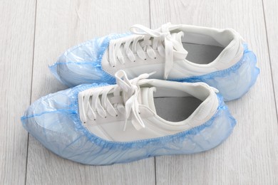 Photo of Sneakers in blue shoe covers on light wooden floor