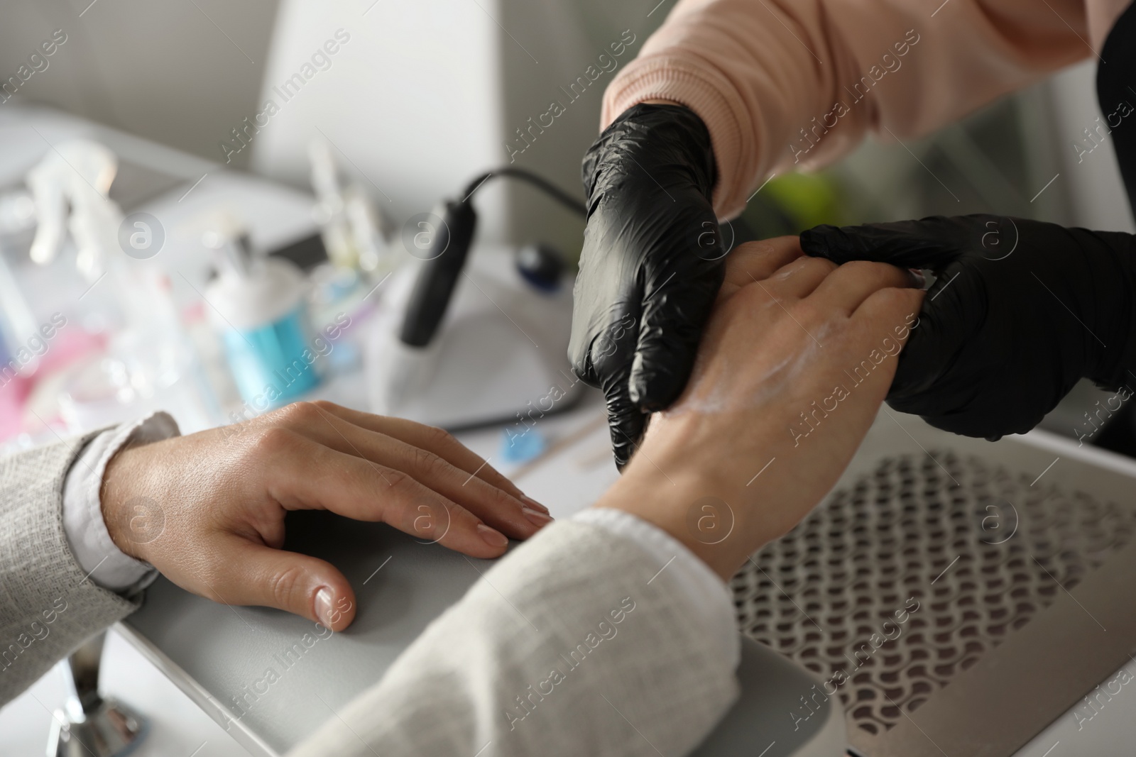 Photo of Professional manicurist applying cream on client's hand in beauty salon, closeup