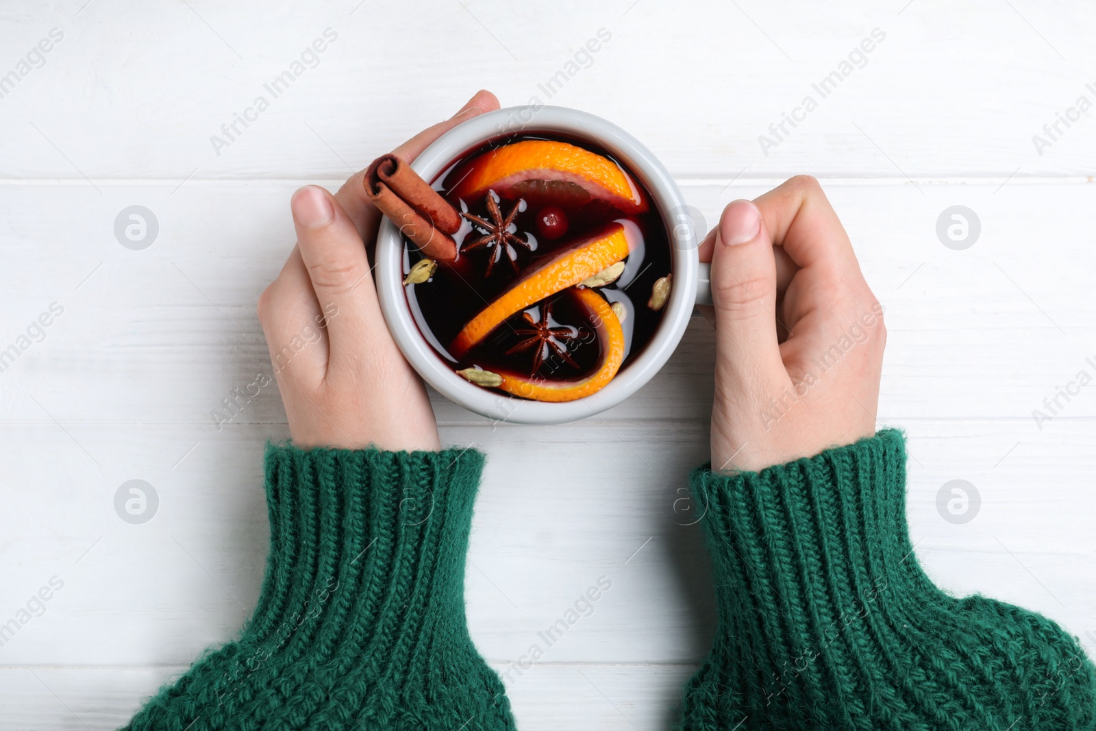 Photo of Woman with cup of mulled wine at white wooden table, top view