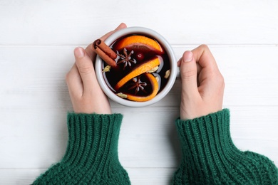Photo of Woman with cup of mulled wine at white wooden table, top view
